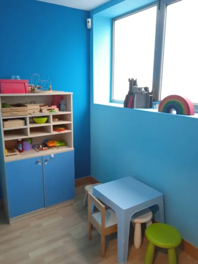 Rincón infantil con mesa pequeña azul, taburetes y estantería con juguetes
